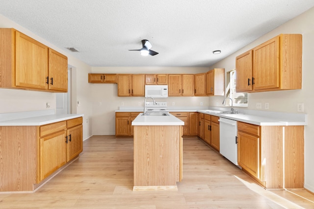 kitchen featuring a kitchen island with sink, sink, white appliances, and light wood-type flooring