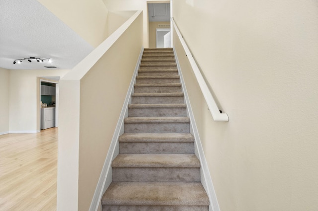 staircase with hardwood / wood-style floors, a textured ceiling, and washer / clothes dryer