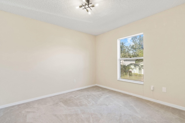 spare room featuring a textured ceiling, light colored carpet, and a notable chandelier