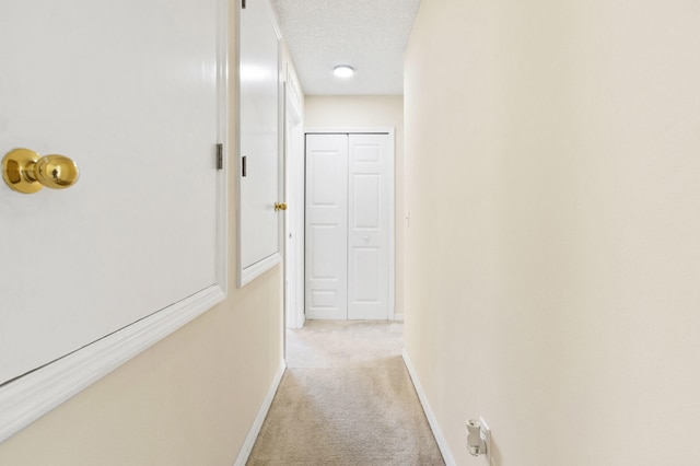 hall with a textured ceiling and light colored carpet