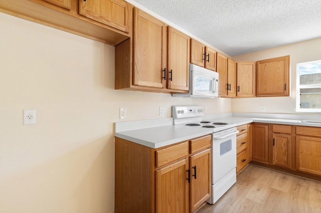 kitchen with a textured ceiling, sink, white appliances, and light wood-type flooring