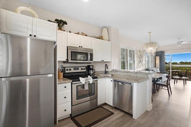 kitchen with kitchen peninsula, hanging light fixtures, appliances with stainless steel finishes, light stone countertops, and white cabinets