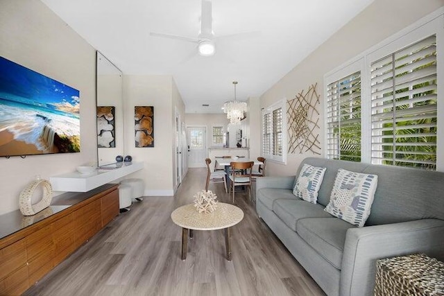 living room with ceiling fan with notable chandelier and light hardwood / wood-style flooring