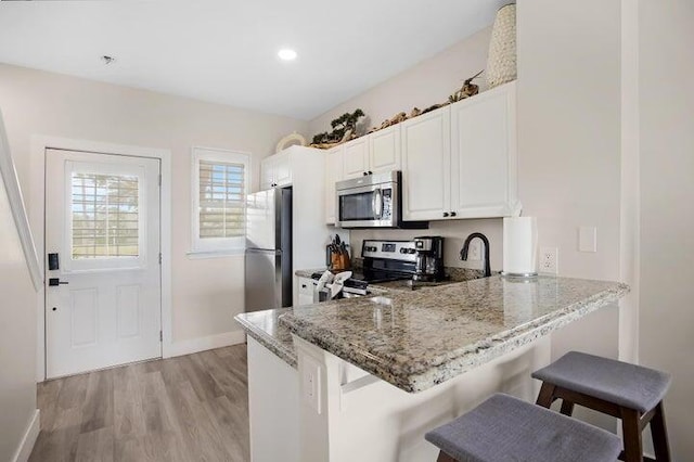 kitchen with kitchen peninsula, a kitchen bar, stainless steel appliances, white cabinets, and stone countertops