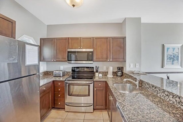 kitchen with sink, light tile patterned floors, stone counters, and appliances with stainless steel finishes