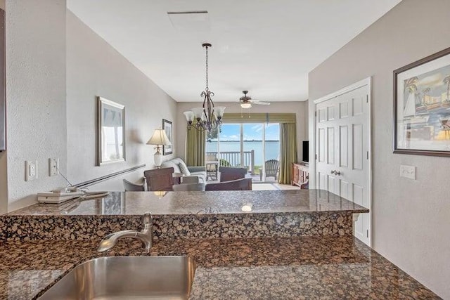 kitchen with ceiling fan with notable chandelier, dark stone counters, pendant lighting, and sink