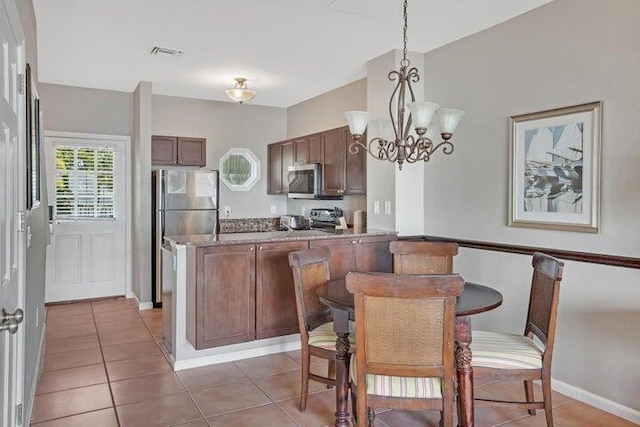 kitchen featuring kitchen peninsula, a chandelier, pendant lighting, light tile patterned floors, and appliances with stainless steel finishes