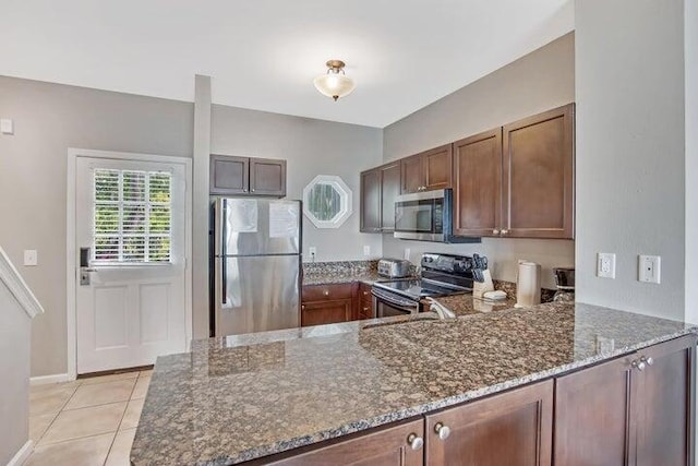 kitchen featuring kitchen peninsula, dark stone counters, appliances with stainless steel finishes, and light tile patterned floors