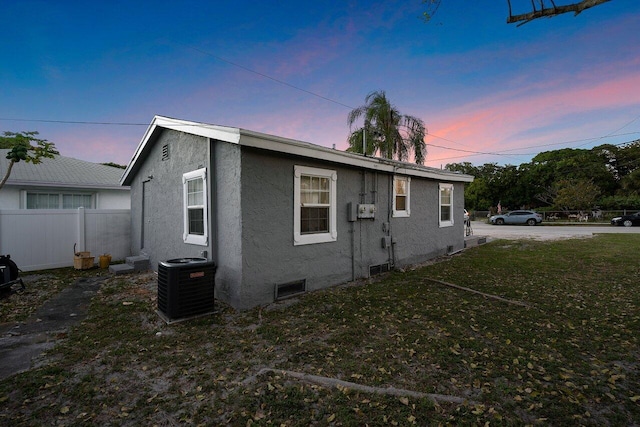 property exterior at dusk with central AC and a lawn