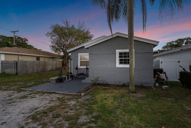 back house at dusk featuring a yard and a patio