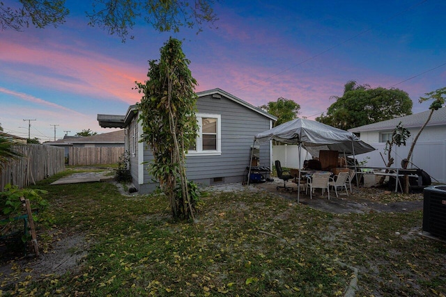 back house at dusk featuring central AC, a yard, and a patio