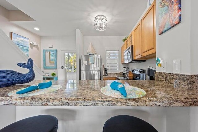 kitchen featuring light brown cabinets, kitchen peninsula, appliances with stainless steel finishes, and light stone counters