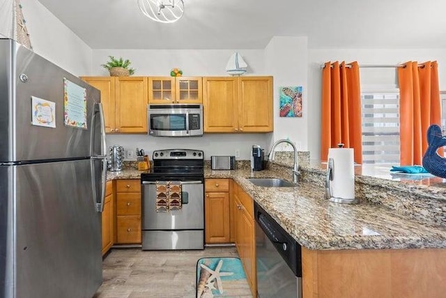 kitchen featuring light hardwood / wood-style floors, kitchen peninsula, appliances with stainless steel finishes, light stone countertops, and sink