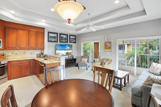 kitchen with light colored carpet, light stone countertops, stainless steel appliances, and a tray ceiling