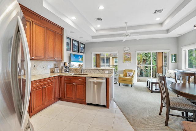 kitchen with kitchen peninsula, appliances with stainless steel finishes, light carpet, a raised ceiling, and sink