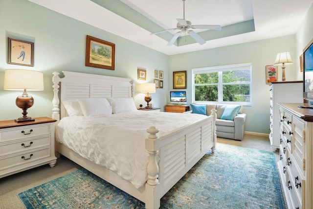 carpeted bedroom featuring ceiling fan and a tray ceiling