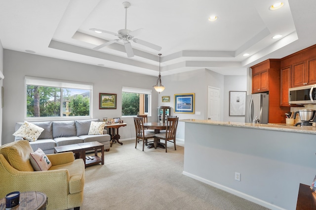 carpeted living room with a raised ceiling and ceiling fan