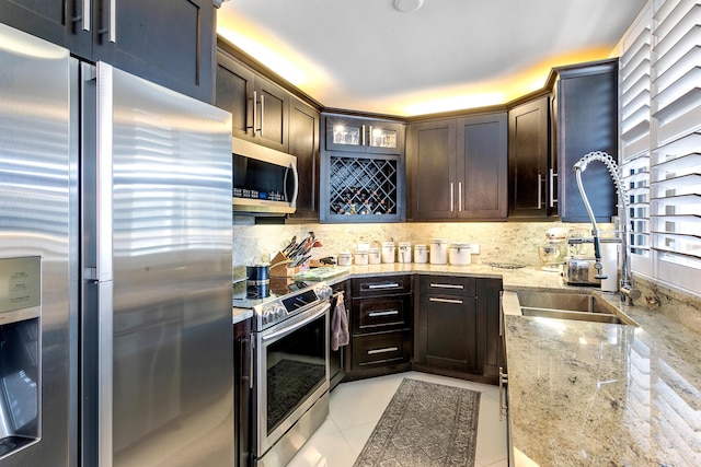 kitchen featuring light stone countertops, tasteful backsplash, dark brown cabinets, light tile patterned floors, and appliances with stainless steel finishes