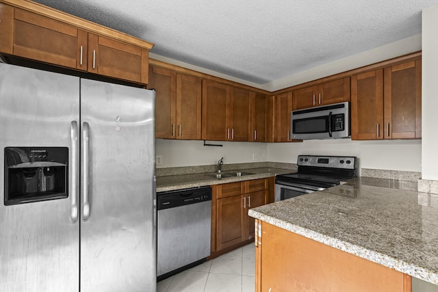 kitchen with dark stone counters, sink, stainless steel appliances, and a textured ceiling