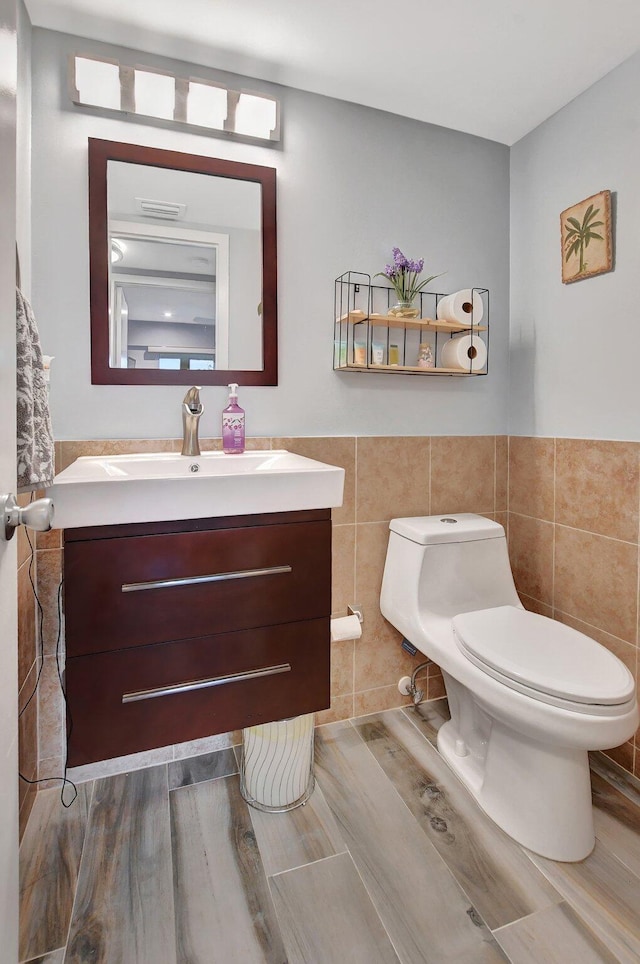 bathroom featuring vanity, toilet, wood-type flooring, and tile walls