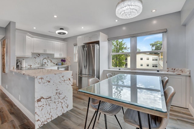 kitchen with white cabinets, hardwood / wood-style flooring, light stone counters, and stainless steel refrigerator