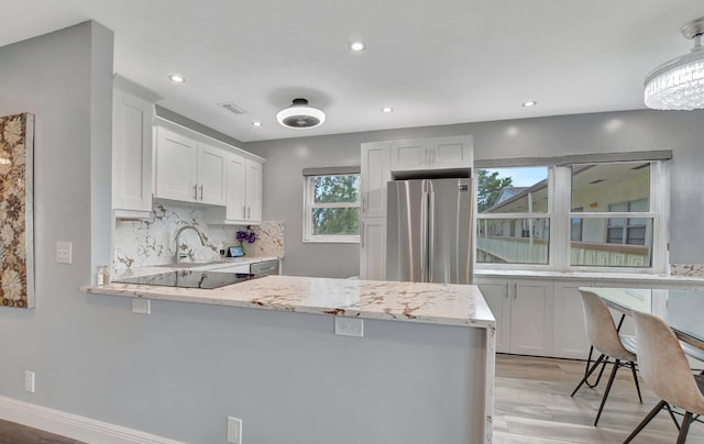 kitchen with kitchen peninsula, stainless steel fridge, white cabinets, and light stone counters