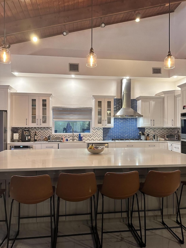 kitchen with wall chimney exhaust hood, glass insert cabinets, decorative light fixtures, light countertops, and a kitchen bar