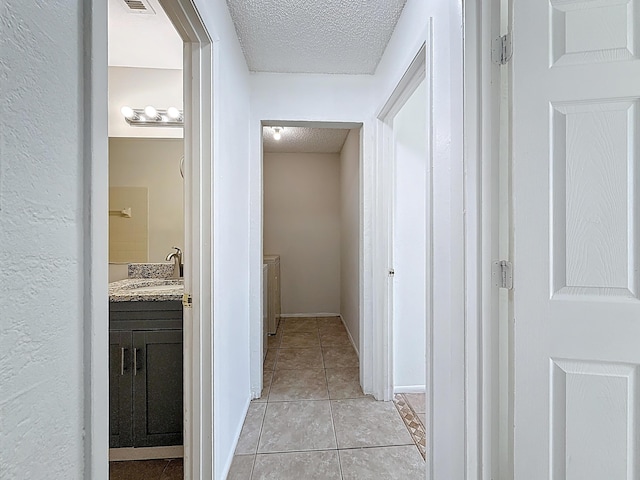 hallway featuring a sink, light tile patterned flooring, a textured ceiling, and visible vents