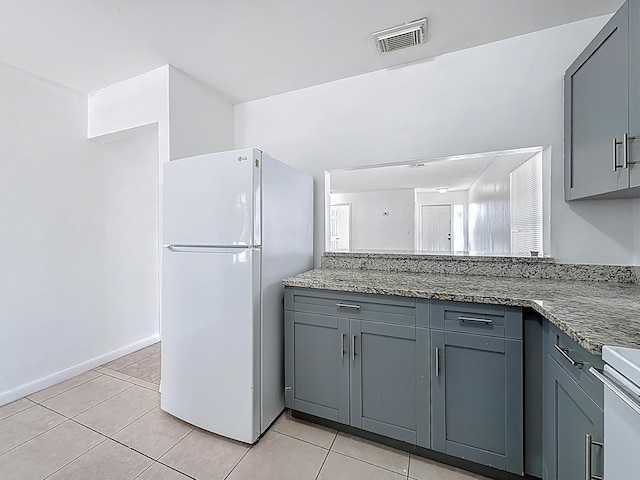 kitchen featuring gray cabinetry, light tile patterned floors, freestanding refrigerator, and visible vents
