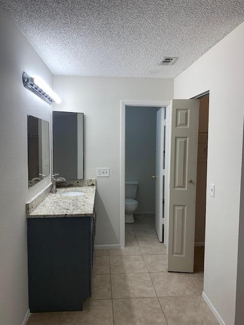 bathroom with tile patterned flooring, vanity, toilet, and a textured ceiling