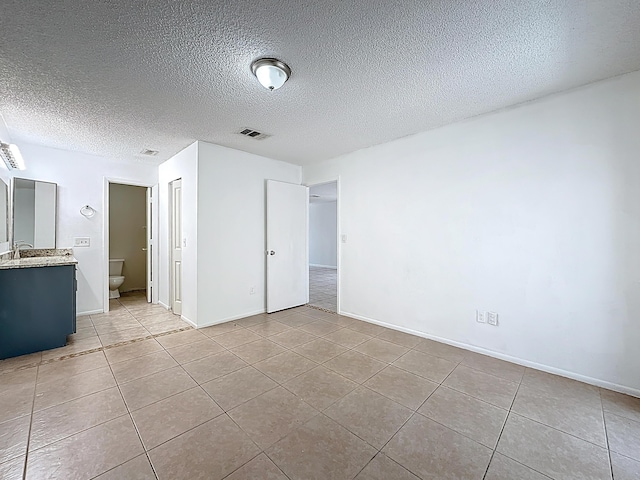 unfurnished bedroom with baseboards, a textured ceiling, visible vents, and light tile patterned floors