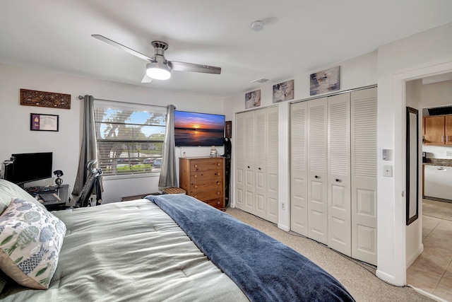 bedroom with ceiling fan, light tile patterned floors, and multiple closets