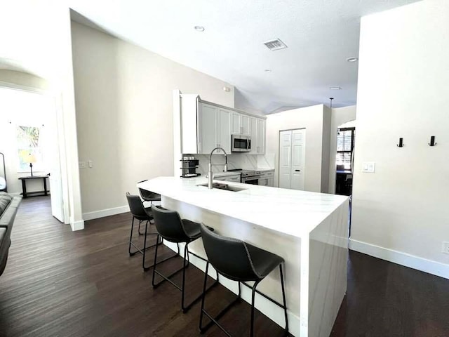 kitchen with a kitchen bar, sink, appliances with stainless steel finishes, dark hardwood / wood-style flooring, and kitchen peninsula