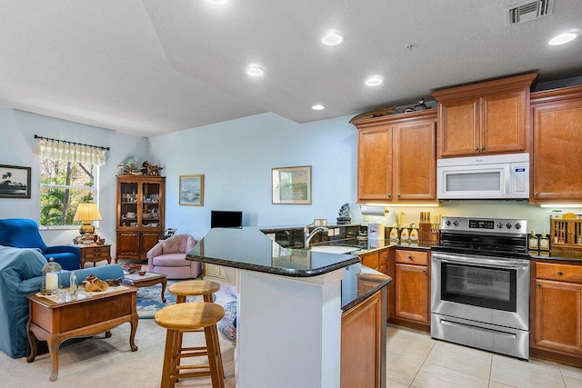 kitchen featuring sink, light tile patterned floors, a textured ceiling, a breakfast bar area, and stainless steel range with electric cooktop