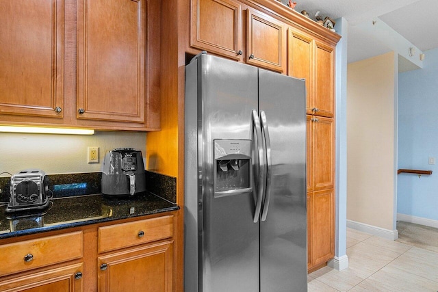 kitchen featuring stainless steel refrigerator with ice dispenser, light tile patterned floors, and dark stone countertops