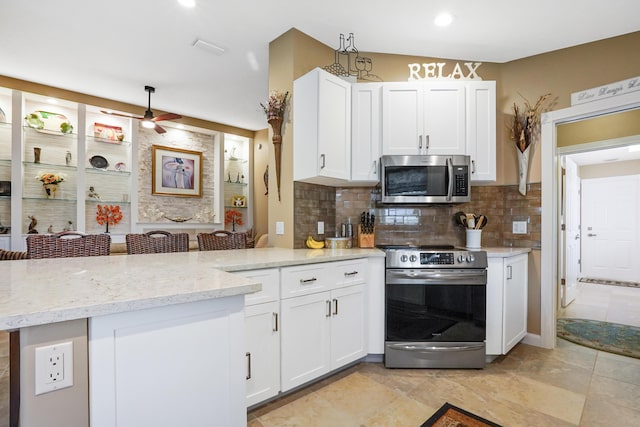 kitchen with kitchen peninsula, appliances with stainless steel finishes, tasteful backsplash, white cabinetry, and a breakfast bar area