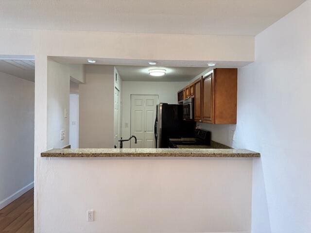 kitchen with kitchen peninsula, stainless steel appliances, light stone counters, and hardwood / wood-style flooring