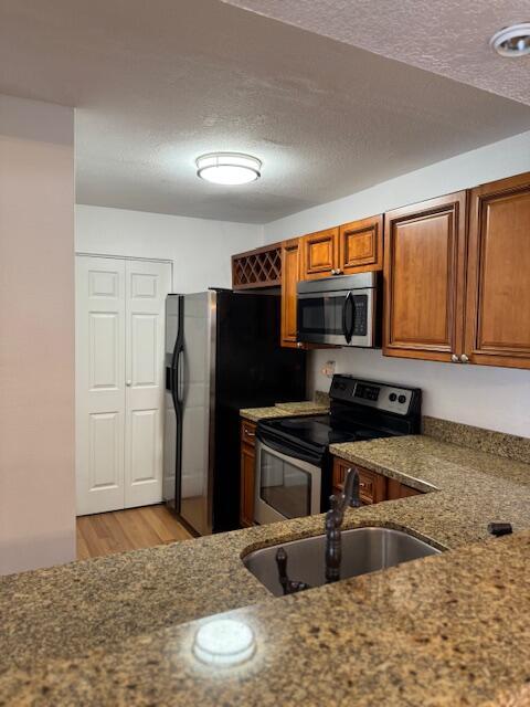 kitchen with light stone countertops, sink, stainless steel appliances, light hardwood / wood-style flooring, and a textured ceiling