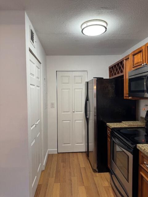 kitchen featuring appliances with stainless steel finishes, a textured ceiling, light hardwood / wood-style flooring, and light stone counters