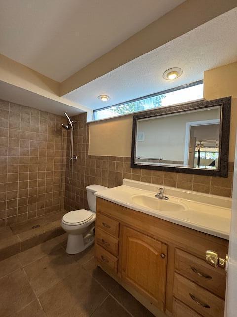 bathroom with tile patterned floors, a tile shower, vanity, tile walls, and toilet