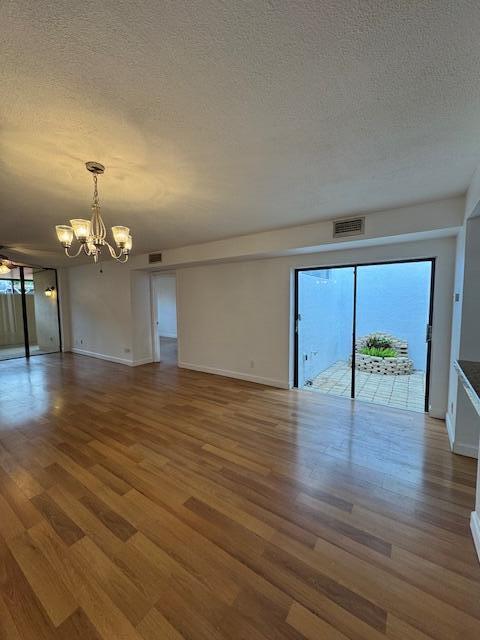 empty room featuring ceiling fan with notable chandelier, wood-type flooring, and a textured ceiling