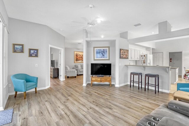 living area with visible vents, baseboards, lofted ceiling, ceiling fan, and light wood-type flooring