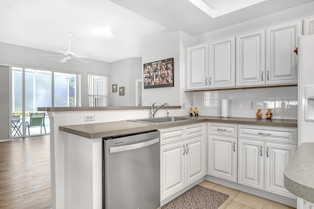 kitchen with a peninsula, a sink, white cabinetry, dishwasher, and dark countertops