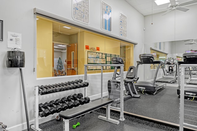 exercise room featuring a ceiling fan, a drop ceiling, and a towering ceiling