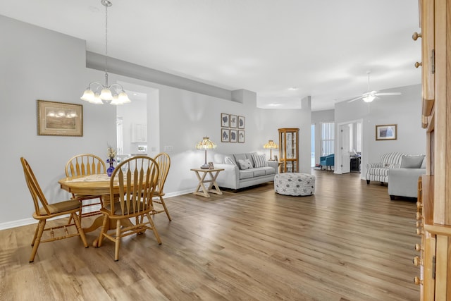 dining room with ceiling fan with notable chandelier, wood finished floors, and baseboards