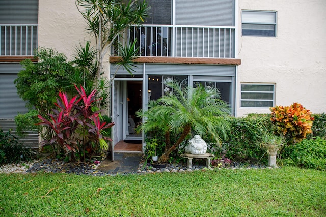 view of exterior entry featuring a balcony and a yard