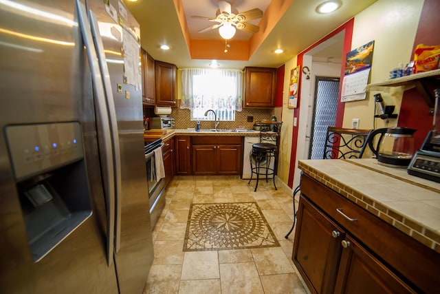 kitchen with sink, tasteful backsplash, tile countertops, stainless steel fridge, and a raised ceiling