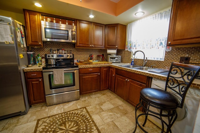 kitchen featuring sink, a breakfast bar, appliances with stainless steel finishes, backsplash, and tile counters