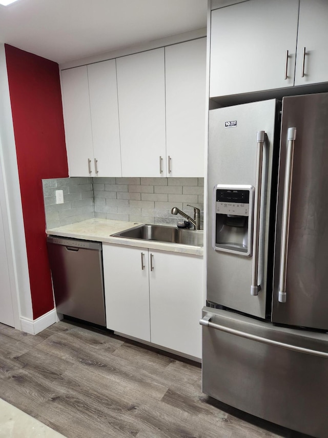 kitchen featuring light wood-type flooring, tasteful backsplash, stainless steel appliances, sink, and white cabinetry