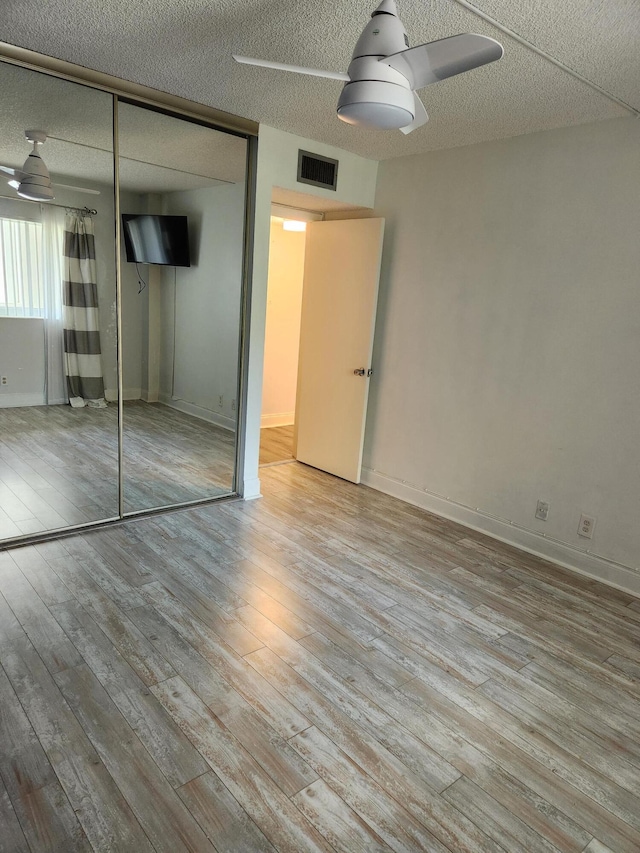 unfurnished bedroom featuring a textured ceiling, light hardwood / wood-style flooring, a closet, and ceiling fan